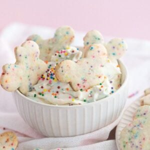 Bowl of funfetti Dunkaroo dip with colorful sprinkle cookies shaped like teddy bears on a pink background.