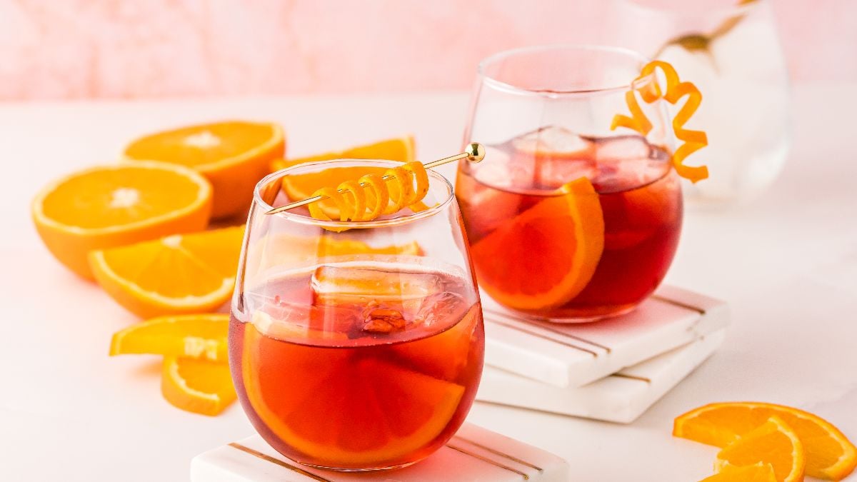Two glasses of negroni cocktail with ice and orange garnishes, surrounded by sliced oranges on a white surface—a classic Italian cocktail perfect for learning how to make the best negroni at home.