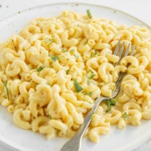 A plate of creamy mac and cheese garnished with herbs, with a fork resting on the side—perfect for anyone craving comfort food or looking for a quick macaroni Instant Pot recipe.