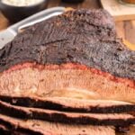 Mesquite smoked brisket, sliced on a wooden cutting board with a knife in the background, showcases the perfect dry rub for brisket and rich flavor from a Traeger grill.