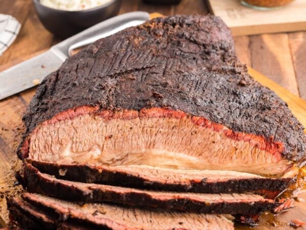 Mesquite smoked brisket, sliced on a wooden cutting board with a knife in the background, showcases the perfect dry rub for brisket and rich flavor from a Traeger grill.