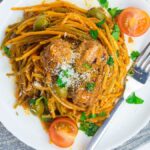 Plate of Mediterranean spaghetti and meatballs, topped with tomato sauce, olives, cherry tomatoes, parsley, and grated cheese.
