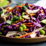 A plate of salad with shredded purple cabbage, carrots, edamame, avocado slices, and herbs—perfect as a refreshing cabbage salad recipe with a drizzle of honey ginger dressing.