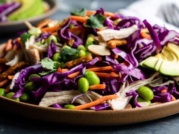 A plate of salad with shredded purple cabbage, carrots, edamame, avocado slices, and herbs—perfect as a refreshing cabbage salad recipe with a drizzle of honey ginger dressing.