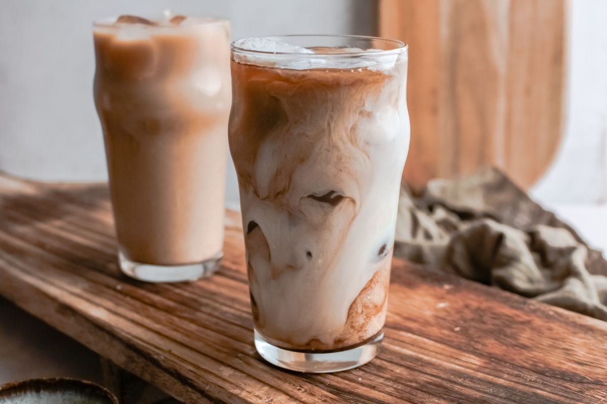 Two glasses of iced coffee with milk, featuring homemade brown sugar syrup, sit on a rustic wooden board. Make a Starbucks iced drink at home and enjoy DIY Starbucks shaken espresso vibes anytime.