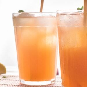 Two glasses of iced peach tea with straws sit beside a lemon wedge and mint—a refreshing DIY Starbucks lemonade recipe perfect for summer sipping.