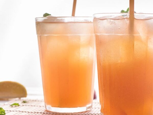 Two glasses of iced peach tea with straws sit beside a lemon wedge and mint—a refreshing DIY Starbucks lemonade recipe perfect for summer sipping.