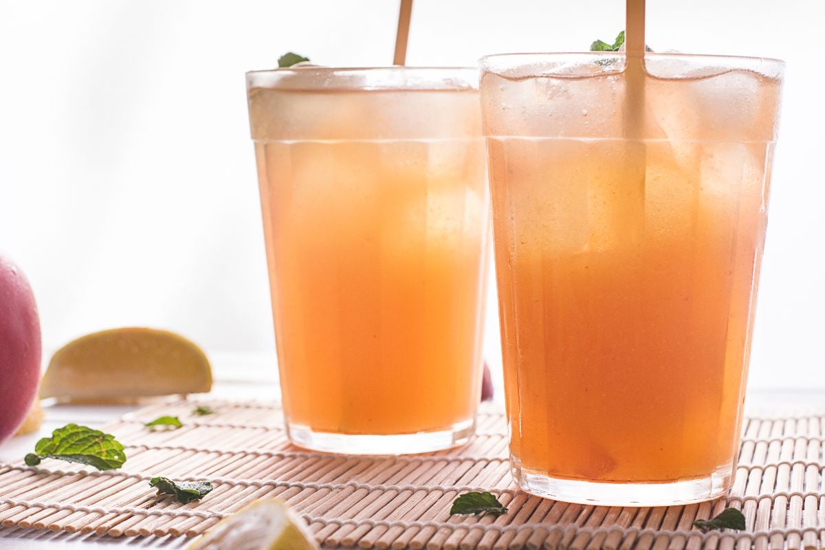 Two glasses of homemade Starbucks peach tea with mint leaves and lemon wedges sit on a bamboo mat—a refreshing Starbucks copycat peach black tea lemonade for summer days.