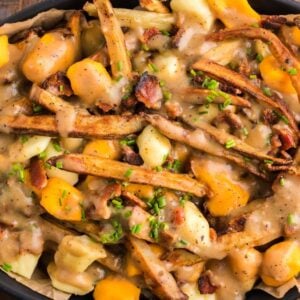 A dish of Canadian poutine featuring fries, cheese curds, savory gravy, and chopped herbs on top.