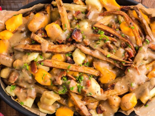 A dish of Canadian poutine featuring fries, cheese curds, savory gravy, and chopped herbs on top.