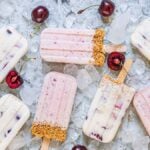 Assorted cherry dessert popsicles with graham cracker crumbs on ice, surrounded by fresh cherries—an irresistible summer treat recipe.