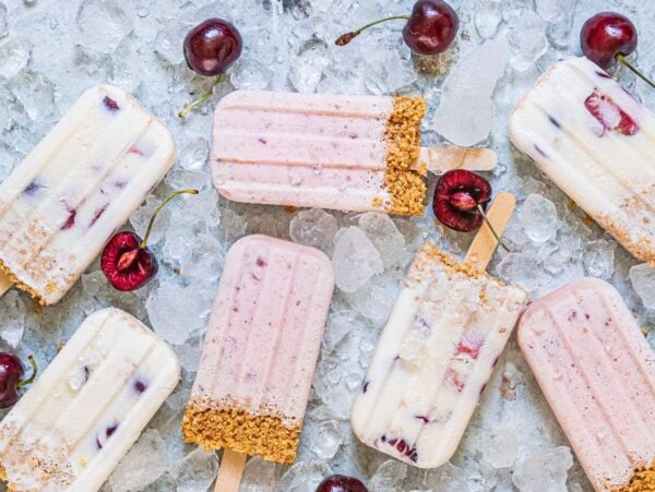 Assorted cherry dessert popsicles with graham cracker crumbs on ice, surrounded by fresh cherries—an irresistible summer treat recipe.