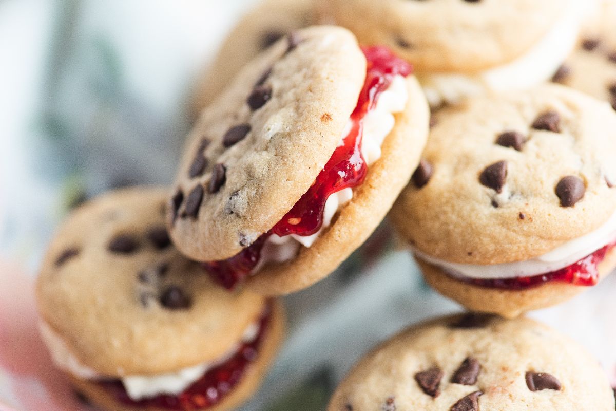 Chocolate chip cookie sandwiches filled with cream and red jam, stacked closely together, make some of the best sandwich cookies with jam.
