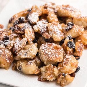 Golden fried Gluten Free Kaiserschmarrn pieces with raisins, dusted with powdered sugar and served on a white square plate—a delicious gluten free dessert pancake.