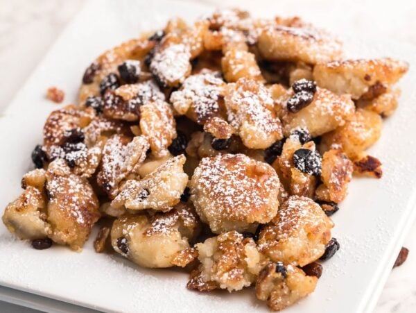 Golden fried Gluten Free Kaiserschmarrn pieces with raisins, dusted with powdered sugar and served on a white square plate—a delicious gluten free dessert pancake.