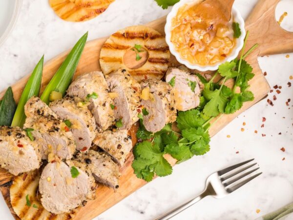 Sliced grilled pork with pineapple, cilantro, and sauce on a wooden board with a fork on the side—an easy Instant Pot Hawaiian pork tenderloin for a delicious Hawaiian inspired recipe.