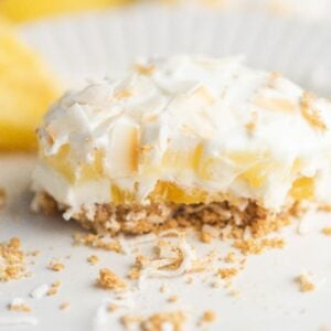 A creamy pineapple lush dessert with a crumbly crust and coconut flakes on a white plate—an easy no bake cake recipe perfect as a dessert for a summer BBQ.