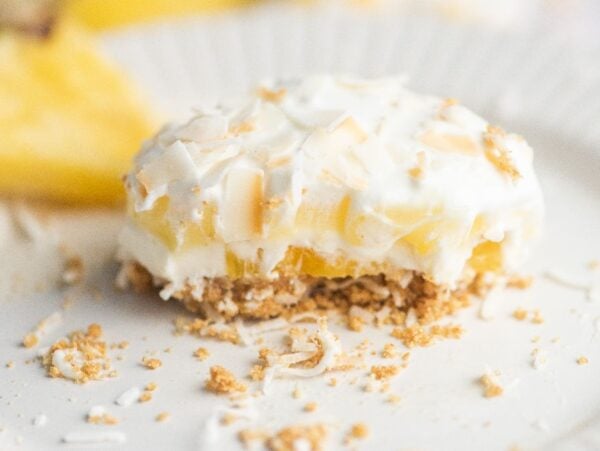 A creamy pineapple lush dessert with a crumbly crust and coconut flakes on a white plate—an easy no bake cake recipe perfect as a dessert for a summer BBQ.