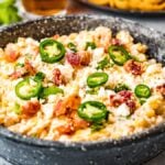 A bowl of creamy jalapeño corn dip topped with bacon, cheese, and cilantro, served with lime wedges on the side—a delicious slow cooker dip recipe perfect for any gathering.