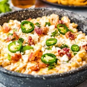 A bowl of creamy jalapeño corn dip topped with bacon, cheese, and cilantro, served with lime wedges on the side—a delicious slow cooker dip recipe perfect for any gathering.