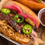 Smoked Brisket Sandwich with sliced brisket, jalapeños, pickles, onions, and crispy fries, served with barbecue sauce—the Best BBQ brisket sandwich experience.