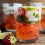 Three glasses of strawberry mojito with ice, mint, lime slices, and strawberries on a wooden surface—an easy summer cocktail recipe perfect for any occasion. Try it as a refreshing cocktail with white rum for a tropical twist.