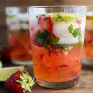 Three glasses of strawberry mojito with ice, mint, lime slices, and strawberries on a wooden surface—an easy summer cocktail recipe perfect for any occasion. Try it as a refreshing cocktail with white rum for a tropical twist.