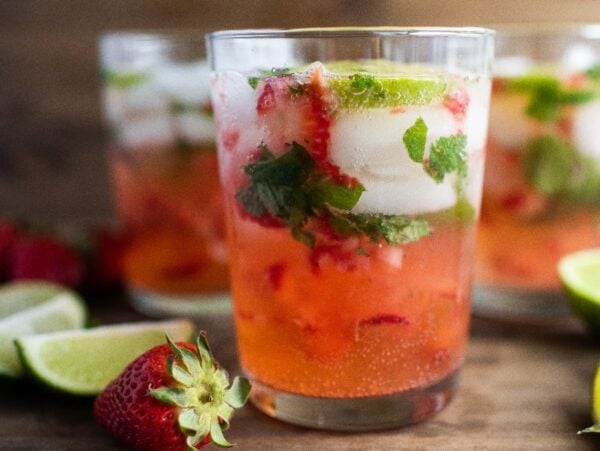Three glasses of strawberry mojito with ice, mint, lime slices, and strawberries on a wooden surface—an easy summer cocktail recipe perfect for any occasion. Try it as a refreshing cocktail with white rum for a tropical twist.