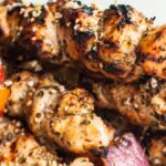 Grilled chicken and vegetable kebabs on skewers, with visible char marks and seasoning, feature a zesty gremolata topping for added freshness.