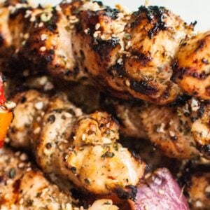 Grilled chicken and vegetable kebabs on skewers, with visible char marks and seasoning, feature a zesty gremolata topping for added freshness.