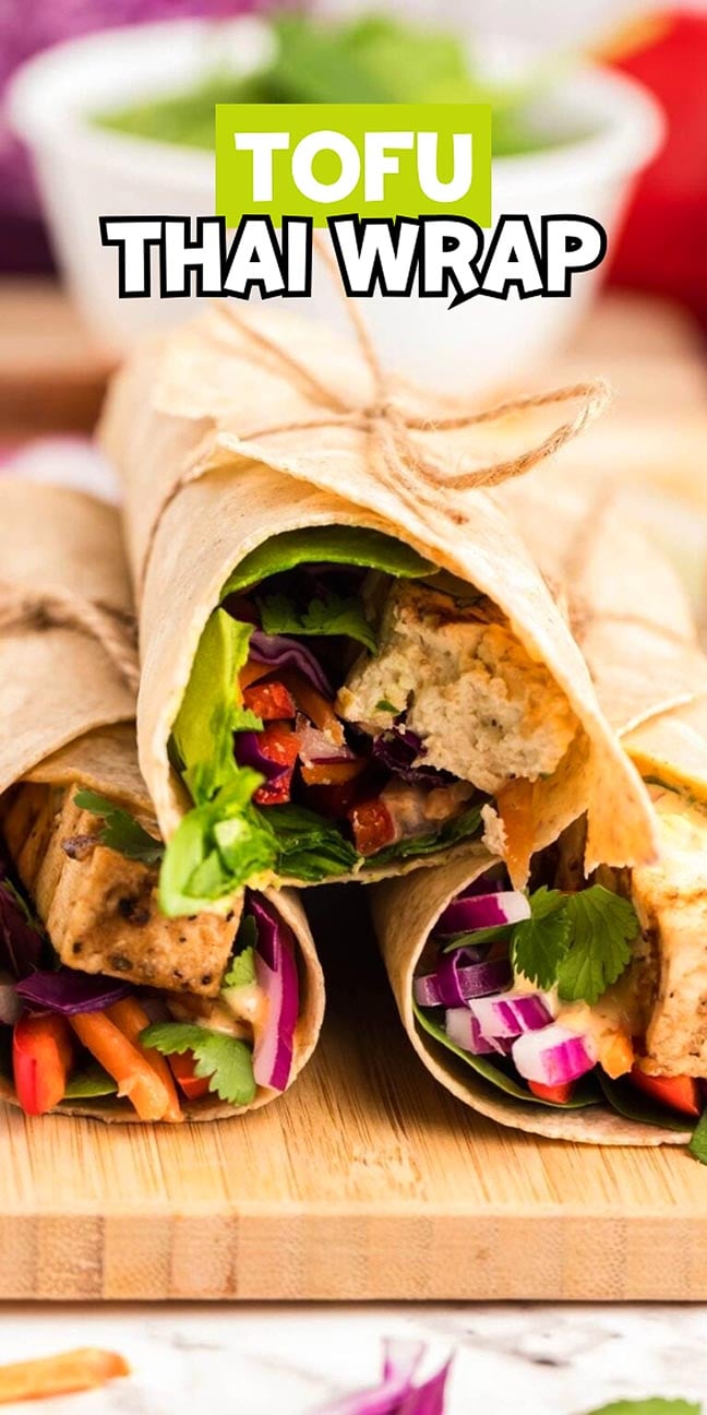 Three tofu Thai wraps with colorful veggies, tied with twine, on a wooden board.