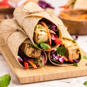 Two Tofu Thai Wraps filled with colorful vegetables and herbs, tied with twine and served on a wooden board—a perfect vegan and gluten free wrap for lunch.