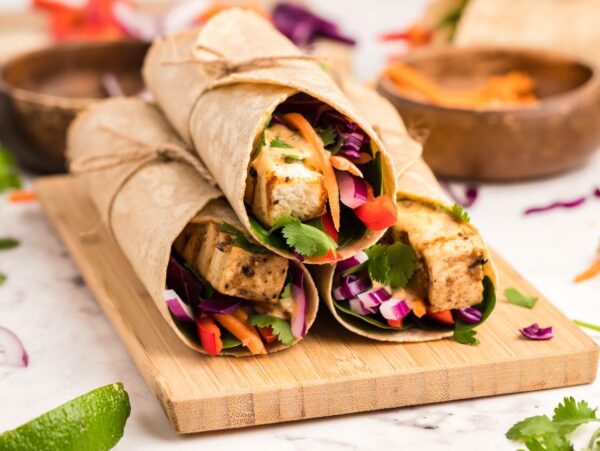 Two Tofu Thai Wraps filled with colorful vegetables and herbs, tied with twine and served on a wooden board—a perfect vegan and gluten free wrap for lunch.