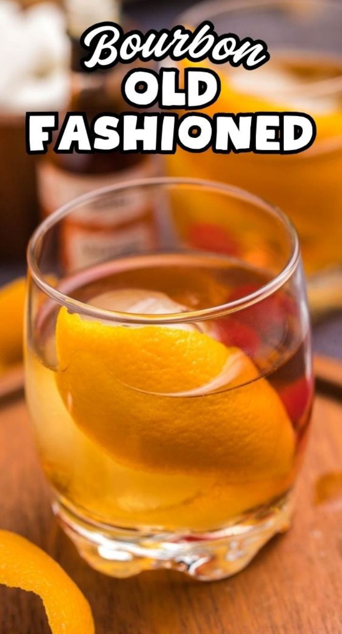 A glass of classic bourbon cocktail, the Bourbon old fashioned, with an orange peel garnish, placed on a wooden surface.