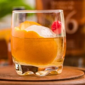 A classic bourbon cocktail, this drink features an orange peel, cherry, and ice ball in a glass on a wooden tray—a timeless bourbon Old Fashioned you can make at home.