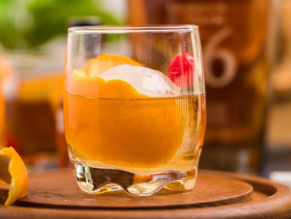 A classic bourbon cocktail, this drink features an orange peel, cherry, and ice ball in a glass on a wooden trayโa timeless bourbon Old Fashioned you can make at home.