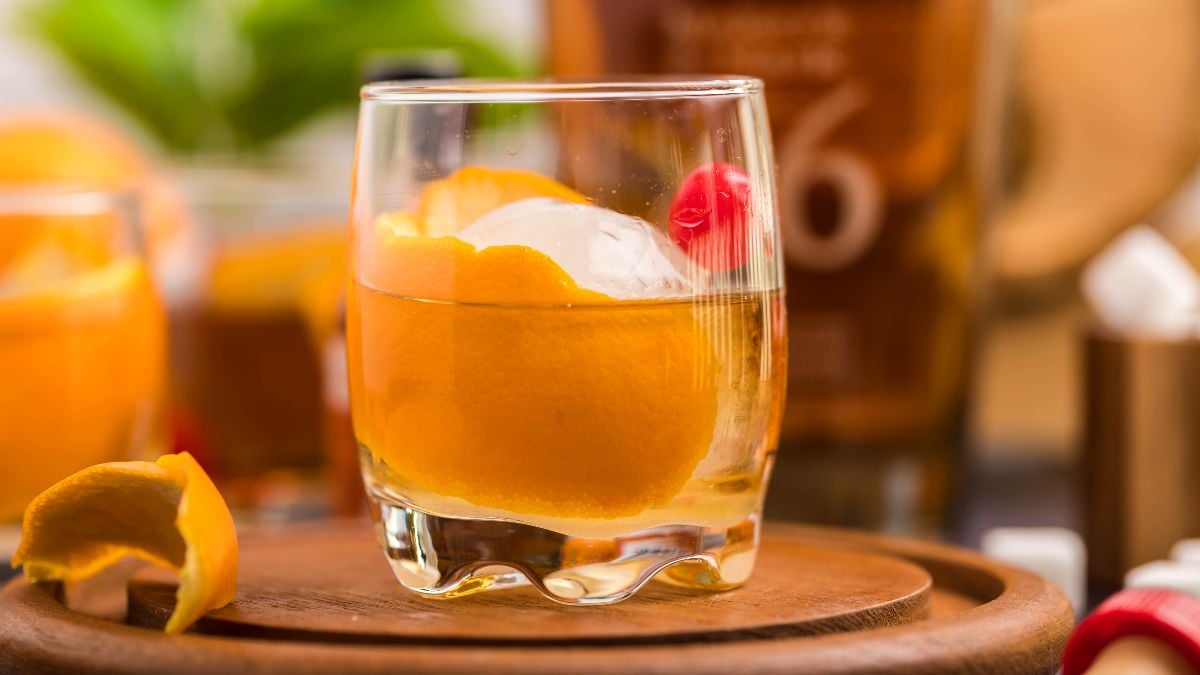 A classic bourbon cocktail, this drink features an orange peel, cherry, and ice ball in a glass on a wooden tray—a timeless bourbon Old Fashioned you can make at home.
