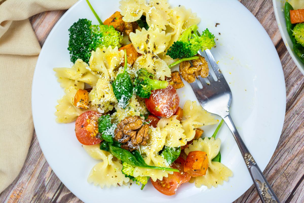 Farfalle pasta with broccoli, cherry tomatoes, walnuts, and grated cheese on a white plate with a fork—perfect for a colorful Butternut Squash and Broccoli Pasta Salad twist.