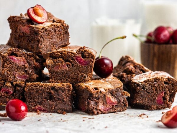 A stack of Fresh cherry brownies with juicy cherries, surrounded by fresh cherries and glasses of milk in the background—an easy cherry dessert perfect for any occasion.