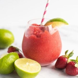 A frozen strawberry lime daiquiri with a striped straw, garnished with lime and surrounded by fresh strawberries and limes—try the best daiquiri recipe for a refreshing rum cocktail delight.