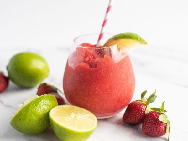 A frozen strawberry lime daiquiri with a striped straw, garnished with lime and surrounded by fresh strawberries and limes—try the best daiquiri recipe for a refreshing rum cocktail delight.