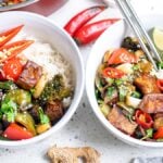 Two bowls of rice topped with Kung Pao Tofu, vibrant vegetables, red chili slices, and lime wedges on a white surface—a perfect Vegetarian Chinese inspired dinner.