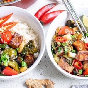 Two bowls of rice topped with Kung Pao Tofu, vibrant vegetables, red chili slices, and lime wedges on a white surface—a perfect Vegetarian Chinese inspired dinner.
