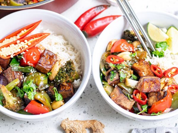 Two bowls of rice topped with Kung Pao Tofu, vibrant vegetables, red chili slices, and lime wedges on a white surface—a perfect Vegetarian Chinese inspired dinner.