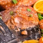 Grilled salmon fillets with sesame seeds, orange slices, and green onions on a tray make for a perfect summer grilled salmon recipe, served alongside vibrant foil packet vegetables.