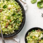 Shaved brussels sprouts and herbs tossed with pistachios make this vibrant Brussels sprouts salad recipe, served in black bowls on a white table with forks—a perfect summer salad recipe.