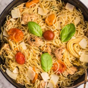 A pot of Sheet Pan Chicken Caprese Pasta with cherry tomatoes, basil leaves, and shaved parmesan on a marble countertop—an easy chicken dinner perfect for any night.