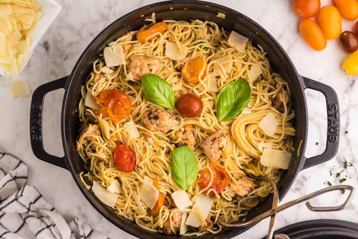 Spaghetti with chicken, cherry tomatoes, basil leaves, and parmesan in a black pot on a marble surface—a perfect easy chicken dinner for any night.