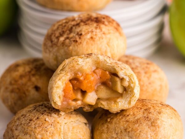 A stack of apple-filled pastry bites, one with a bite showing the spiced filling inside—these puff pastry dumplings are perfect for snacking. Try making Air Fryer Apricot Apple Dumplings for a quick and delicious twist!.
