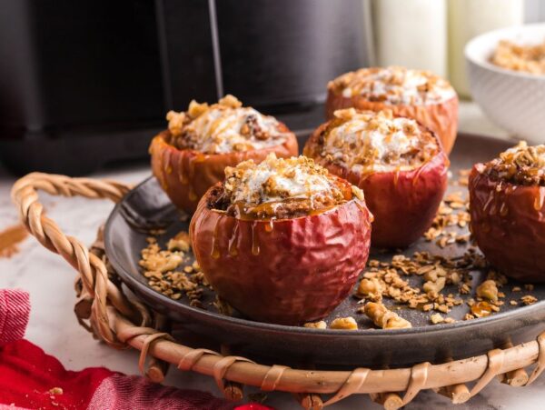 Baked apples stuffed with oats and nuts on a black plate, drizzled with maple syrup, make an easy air fryer apple dessert served on a woven tray.